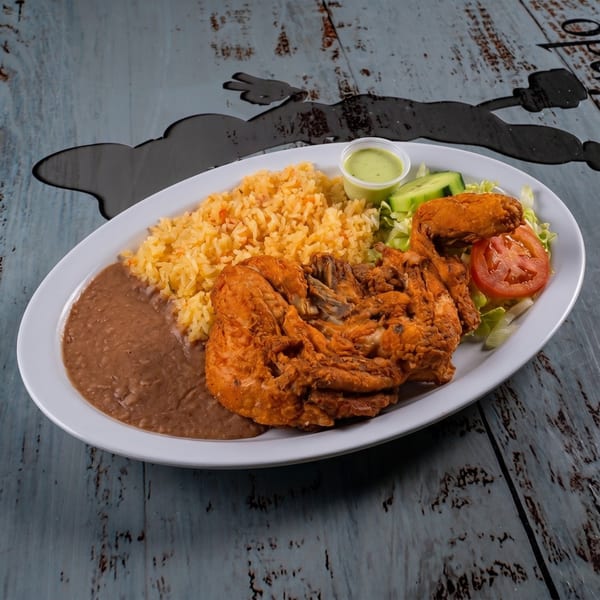 Fried chicken with rice, refried beans, a side salad, and green sauce on a white plate.