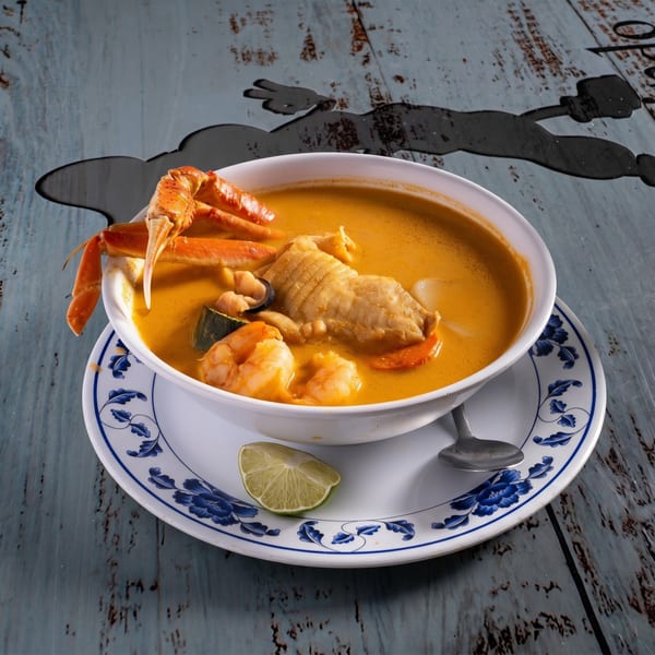 Seafood stew with crab legs, shrimp, fish, and vegetables in a white bowl with a lime wedge.