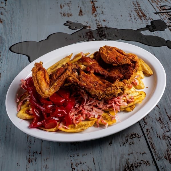 Fried chicken wings, plantain chips, red cabbage slaw, and red sauce on a white plate.