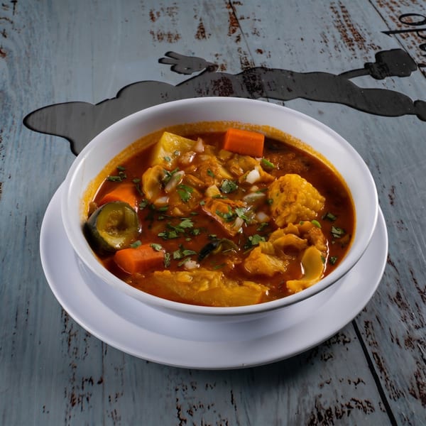 Hearty bowl of menudo soup with vegetables and cilantro on a rustic wooden table.